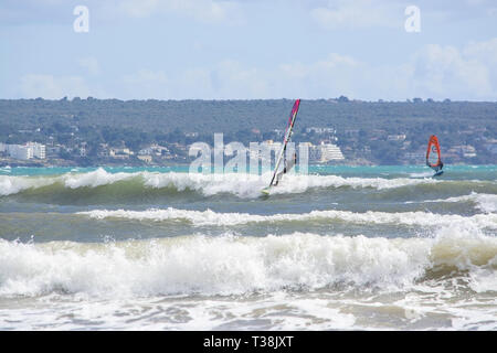 CAN PASTILLA, MALLORCA, SPANIEN - 6. APRIL 2019: Surfer in die grünen Wellen spielen an einem windigen, sonnigen Tag am 6. April 2019 in Can Pastilla, Mallorca, Sp Stockfoto
