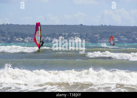 CAN PASTILLA, MALLORCA, SPANIEN - 6. APRIL 2019: Surfer in die grünen Wellen spielen an einem windigen, sonnigen Tag am 6. April 2019 in Can Pastilla, Mallorca, Sp Stockfoto