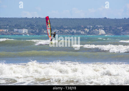 CAN PASTILLA, MALLORCA, SPANIEN - 6. APRIL 2019: Surfer in die grünen Wellen spielen an einem windigen, sonnigen Tag am 6. April 2019 in Can Pastilla, Mallorca, Sp Stockfoto