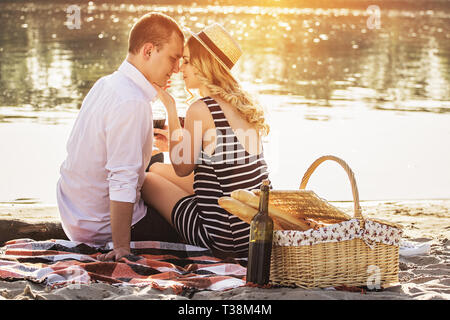 Schöne Liebesgeschichte. Horizontale schoss der schönen jungen Paar Wein trinken und sitzen in der Nähe von Angesicht zu beim romantischen Picknick am Strand Gesicht Stockfoto