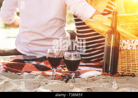 Romantisches date am Strand. 7/8-Ansicht der Rückseite des jungen Mann umarmte seine schöne Freundin im Kleid beim romantischen Picknick im Freien mit evenin Stockfoto