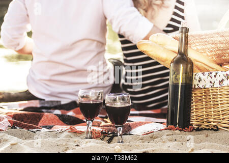 Feiern ihren besonderen Datum. 7/8-Ansicht der Rückseite des jungen Mann umarmte seine schöne Freundin im Kleid beim romantischen Picknick am Strand. Stockfoto