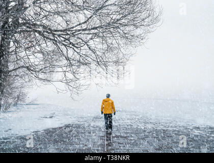 Ein Mann in einer gelben Mantel Wandern auf der schneebedeckten Straße Stockfoto