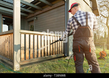 Mann Reinigung mit einem Hochdruckreiniger - hohen Wasserdruck Reiniger auf hölzernen Terrasse Geländer Stockfoto