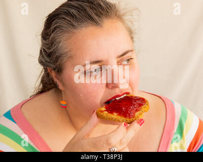 Eine erwachsene Frau mit roten Nägeln und Lippen essen ein Zwieback mit himbeermarmelade Stockfoto