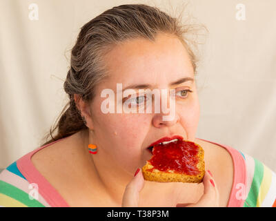 Eine erwachsene Frau mit roten Nägeln und Lippen essen ein Zwieback mit himbeermarmelade Stockfoto