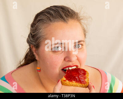 Eine erwachsene Frau mit roten Nägeln und Lippen essen ein Zwieback mit himbeermarmelade Stockfoto