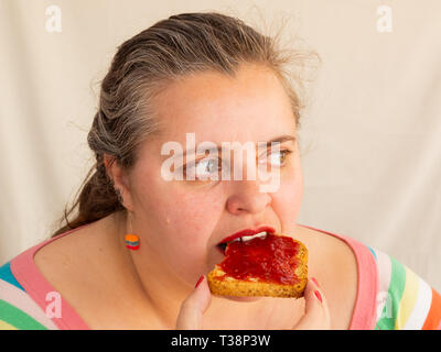 Eine erwachsene Frau mit roten Nägeln und Lippen essen ein Zwieback mit himbeermarmelade Stockfoto