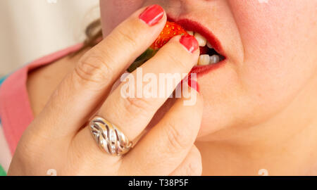 Eine erwachsene Frau mit roten Nägeln und Lippen essen eine Erdbeere Stockfoto