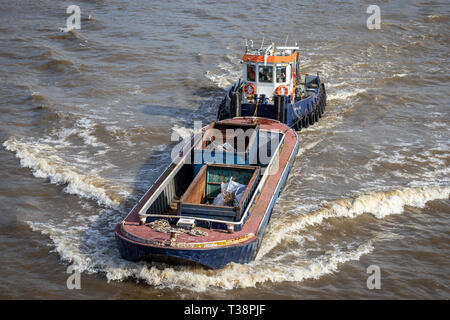 Blick hinunter auf einen Schlepper, der einen großen Frachtschiff mit Abfallstoffen den Fluss entlang schiebt, aufgenommen auf der Themse in London am 26th. April 2019 Stockfoto