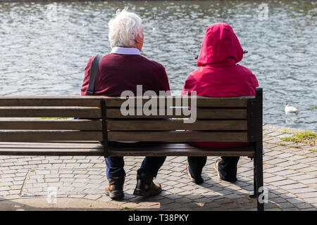 Ältere Paare setzte sich auf eine Holzbank mit Blick auf das Wasser Stockfoto