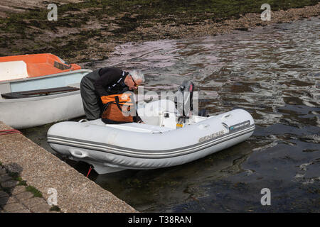 Im mittleren Alter Mann beim Entleeren eines starren Schlauchboot mit Außenbordmotor in Hafen tragen waders Stockfoto