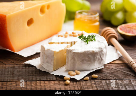 Brie oder Camembert, Scheibe des gelben Käse, Honig, Trauben und Feigen auf einem Holztisch Hintergrund Stockfoto