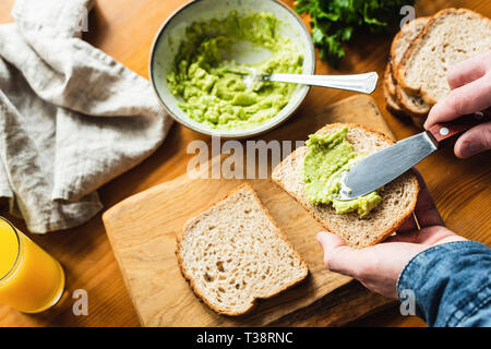 Person, die Avocado Toast mit Guacamole oder Guacamole Sauce auf Vollkorn sandwich Brot Stockfoto