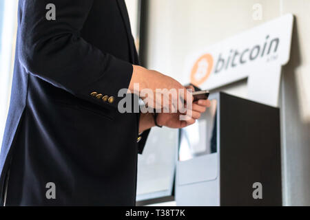 Geschäftsmann Kauf und Übertragung cryptocurrency zu Handy von ATM Maschine für den Kauf und Verkauf von cryptocurrency. Stockfoto