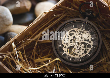 Pocket Watch Winder auf natürlichen Weizen Stroh in einer Holzkiste. Konzept der Vintage oder retro Geschenk. Stockfoto