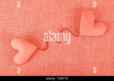 In der Nähe von Coral Pink Farbe GETONTE zwei handgefertigten Filz Spielzeug Herzen mit Garn auf Leinwand Hintergrund, Nahaufnahme, erhöhte Hohe Betrachtungswinkel Stockfoto