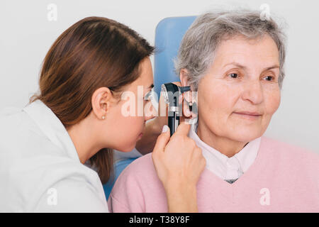 Arzt untersucht ältere Patienten Ohr, mit Otoskop, in der Arztpraxis. Ältere Frau erhalten medizinische Ohr Untersuchung an der Klinik. Stockfoto