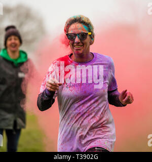 Läuferin lachen und in Farbe auf Macmillan Cancer Charity 5K Farbe Fun Run abgedeckt. Stockfoto