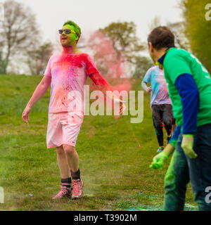 Erwachsene männliche Läufer mit ausgestreckten Armen in Farbe auf Macmillan Cancer Charity 5K Farbe Fun Run abgedeckt. Stockfoto