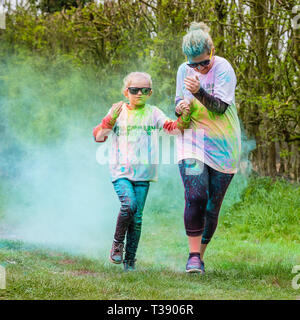 Mutter und Tochter Läufer halten sich an den Händen und in Farbe auf Macmillan Cancer Charity 5K Farbe Fun Run abgedeckt. Stockfoto