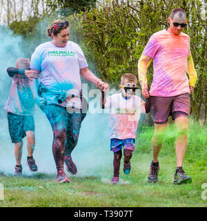 Familie mit zwei Erwachsenen und zwei Kindern in Farbe auf Macmillan Cancer Charity 5K Farbe Fun Run wird abgedeckt. Stockfoto