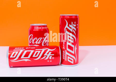 Peniscola, Castellon, Spanien - 07 April 2019: drei Dosen Cola, zwei in Chinesisch geschrieben, Getränke auf einem orange Farbe Hintergrund isoliert. Die nicht-Alcoh Stockfoto