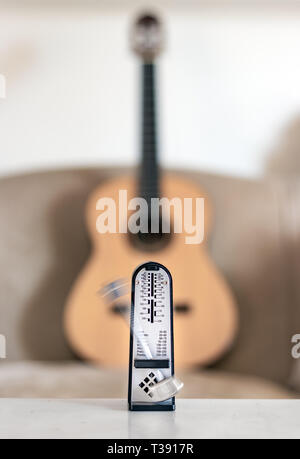 Mechanische Metronome in Bewegung, über eine hölzerne klassische Gitarre Hintergrund. Stockfoto