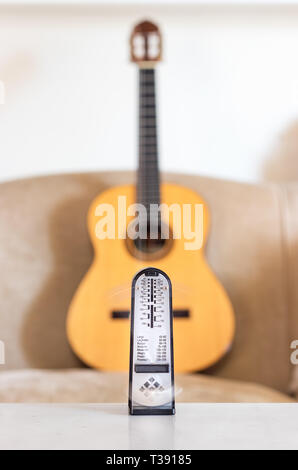 Mechanische Metronome in Bewegung, über eine hölzerne klassische Gitarre Hintergrund. Stockfoto