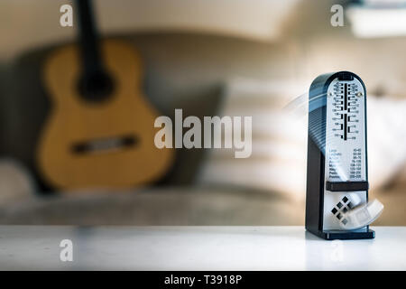 Mechanische Metronome in Bewegung, über eine hölzerne klassische Gitarre Hintergrund. Stockfoto