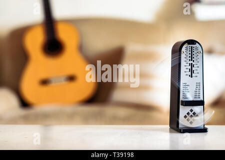 Mechanische Metronome in Bewegung, über eine hölzerne klassische Gitarre Hintergrund. Stockfoto