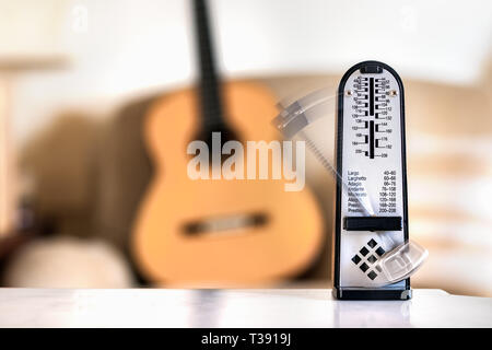 Mechanische Metronome in Bewegung, über eine hölzerne klassische Gitarre Hintergrund. Stockfoto