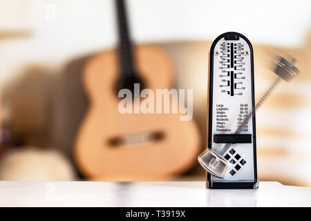 Mechanische Metronome in Bewegung, über eine hölzerne klassische Gitarre Hintergrund. Stockfoto