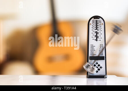 Mechanische Metronome in Bewegung, über eine hölzerne klassische Gitarre Hintergrund. Stockfoto