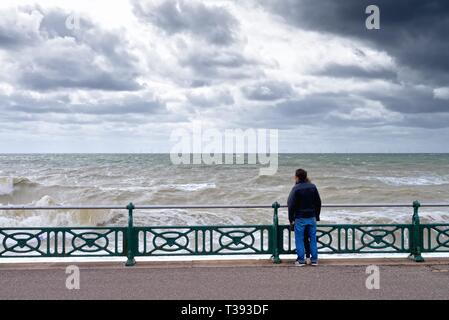 Junges Paar sehr nahe stehen, zusammen mit Blick aufs Meer in einer stürmischen Frühling auf der Strandpromenade Hoves entfernt East Sussex England Großbritannien Stockfoto