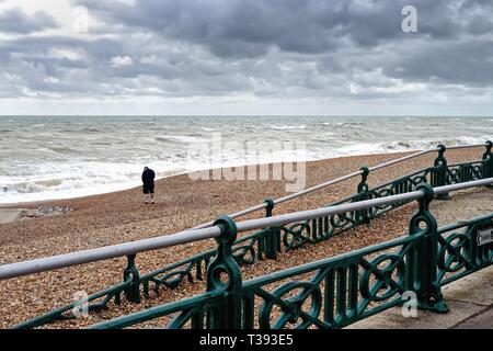 Single einsame männliche Figur am Strand an der Strandpromenade Hoves entfernt an einem stürmischen Frühling, East Sussex England Großbritannien Stockfoto