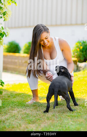 Fröhliche schwangere Frau mit einem großen Bauch spielt mit ihrem Hund in den Garten Stockfoto