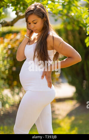 Nachdenklich schwangere Frau im Garten, Hände auf der Rückseite Stockfoto