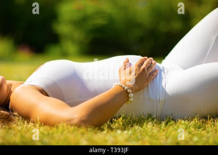 In der Nähe von wunderschönen schwangere Frau in weißen Kleidern Festlegung auf Gras Stockfoto