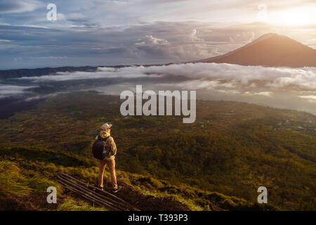 Man touristische sieht bei Sonnenaufgang auf dem Vulkan Batur auf der Insel Blai in Indonesien. Wanderer Mann mit Rucksack Reisen auf Vulkan, Reisen Stockfoto