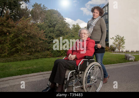 Junge Frau hilft, ältere Frau im Rollstuhl Stockfoto