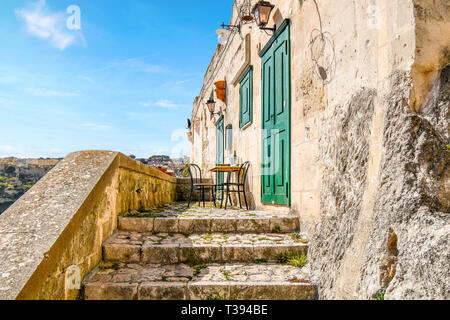 Zwei Stühle und einen Tisch mit einer Flasche Wein sitzen auf einer kleinen Terrasse draußen eine grüne Tür und Verschluss in der antiken Stadt Matera, Italien. Stockfoto