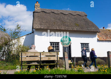 Thriplow, Cambridge, England, UK - März 2019: Älteres Ehepaar sitzt auf einer Holzbank an einem Dorf Bushaltestelle mit traditionellen britischen Cottage Stockfoto