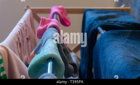 Nicht übereinstimmende, paar Söckchen trocknen auf einem Wäscheständer mit der Kleidung der Frau einschließlich Blue Jeans und Pullover rosa Öse, drinnen im Wohnzimmer. Stockfoto