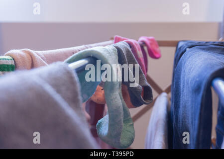 Fokus auf Söckchen trocknen auf einem Wäscheständer mit der Kleidung der anderen Frau, einschließlich Blue Jeans. Nicht zusammenpassende Socken und ein paar abgestimmte Socken. Stockfoto