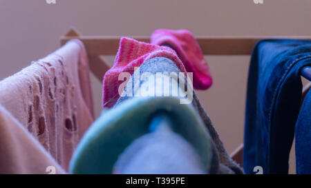 Fokus auf einem rosa Socke trocknen auf einem Wäscheständer mit der Kleidung der anderen Frau, und nicht zusammenpassende Socken verschwommen im Vordergrund. Darstellung Wäscheservice Tag. Stockfoto