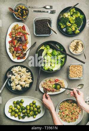 Veganen Abendessen Tabelle einstellen. Gesunde Gerichte in Platten auf Beton. Flachbild-lay von Gemüse Salate, Hülsenfrüchte, Bohnen, Oliven, Sprossen, Hummus und woma Stockfoto