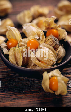 Kap Stachelbeeren (Physalis Rubro) oder Kirschen mit Kelch in der Schüssel auf Holzbrett Stockfoto