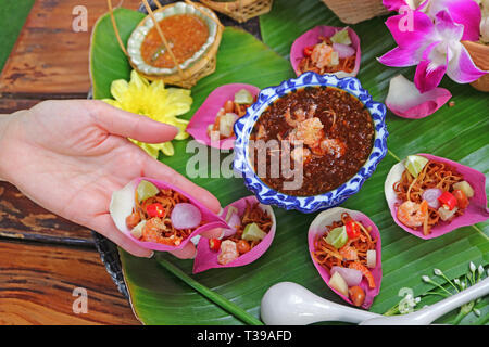 Frau Hand mit einem frischen Lotus Petal herzhaften gewickelt Miang Kham in der thailändischen Sprache namens Stockfoto