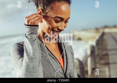 Gesunde junge Frau Musik hören, während an der Promenade zu trainieren. Läuferin Einstellen der Ohrhörer und lächelnd, während sie eine Pause vom Stockfoto